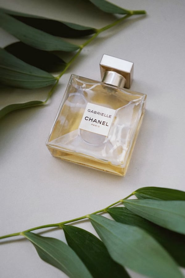 Glass of perfume lying on a white table with branches of leaves